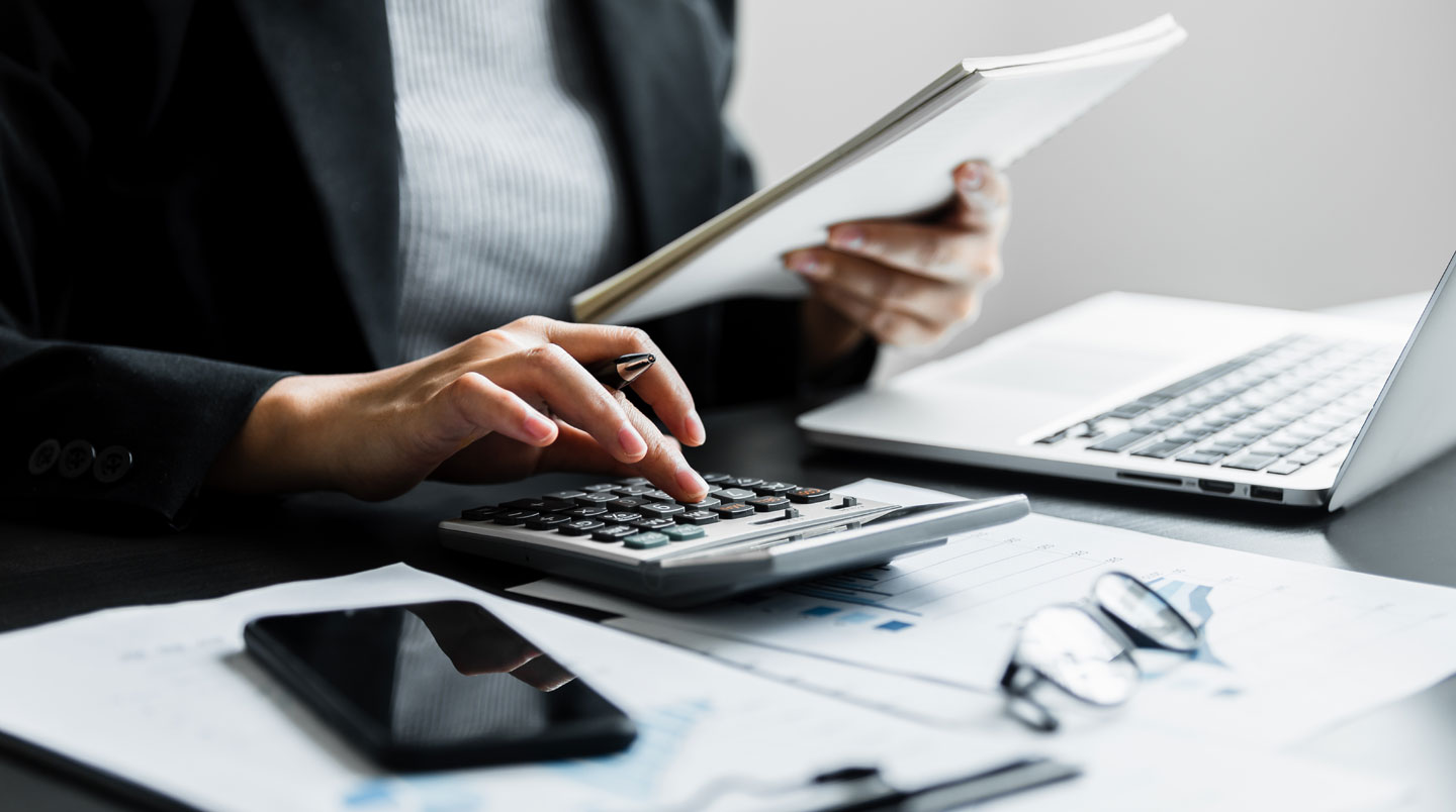 Personne concentrée comparant plusieurs offres de crédit immobilier sur un écran d'ordinateur, bloc-notes avec annotations manuscrites à côté, ambiance de bureau lumineux